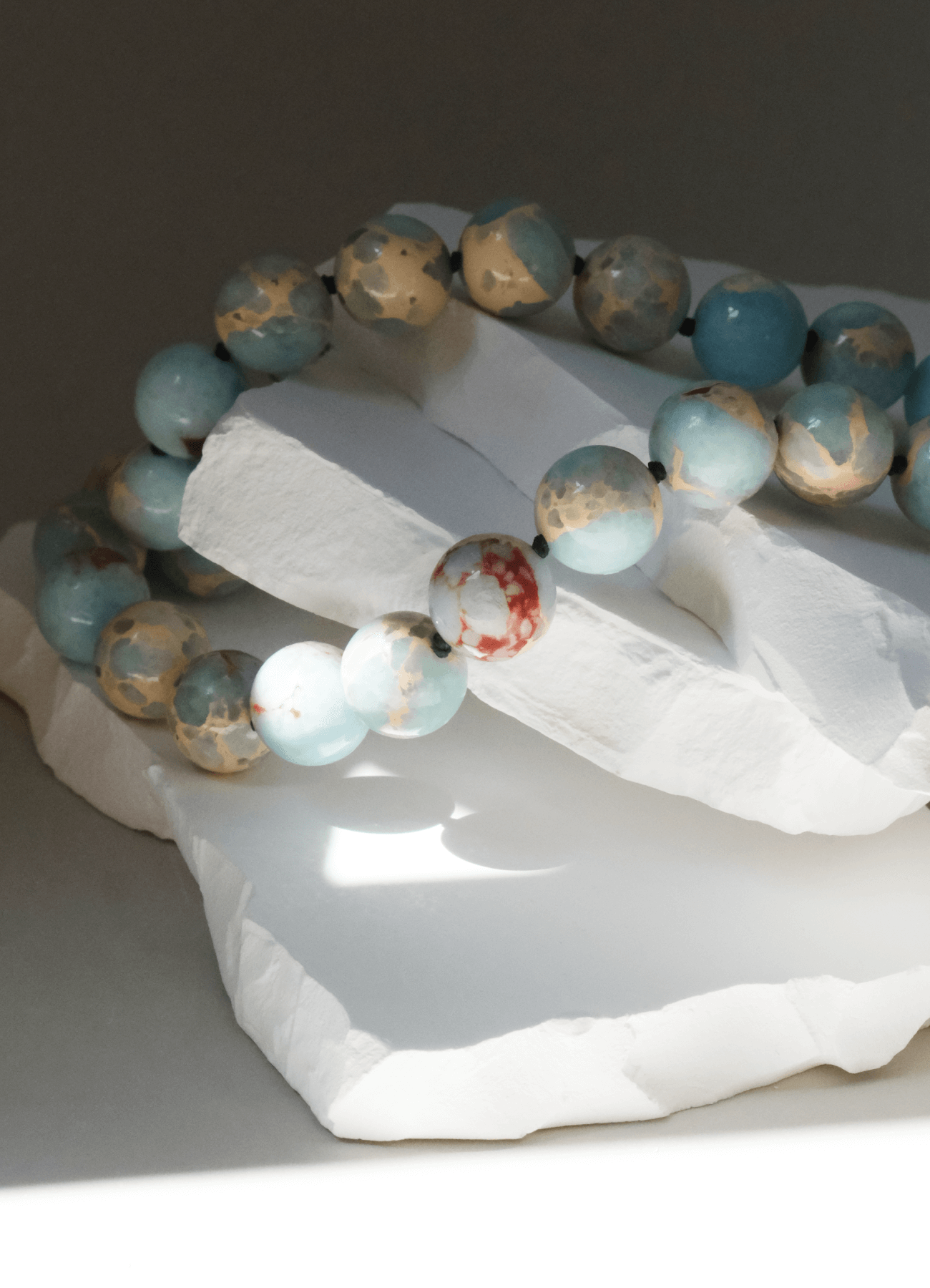 Imperial jasper gemstone necklace lying on white stone sun shadows