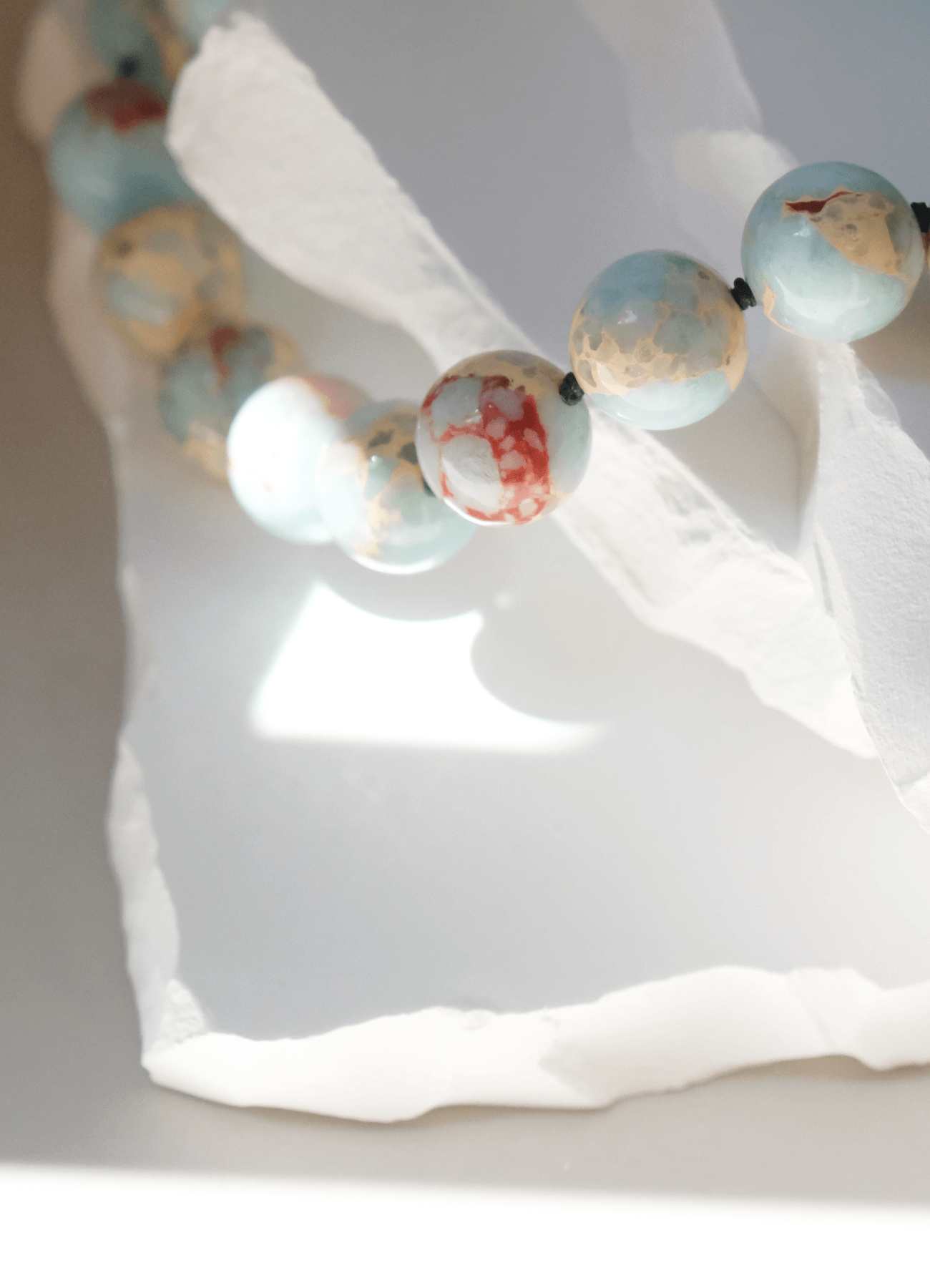 Imperial jasper gemstone necklace lying on white stone sun shadows