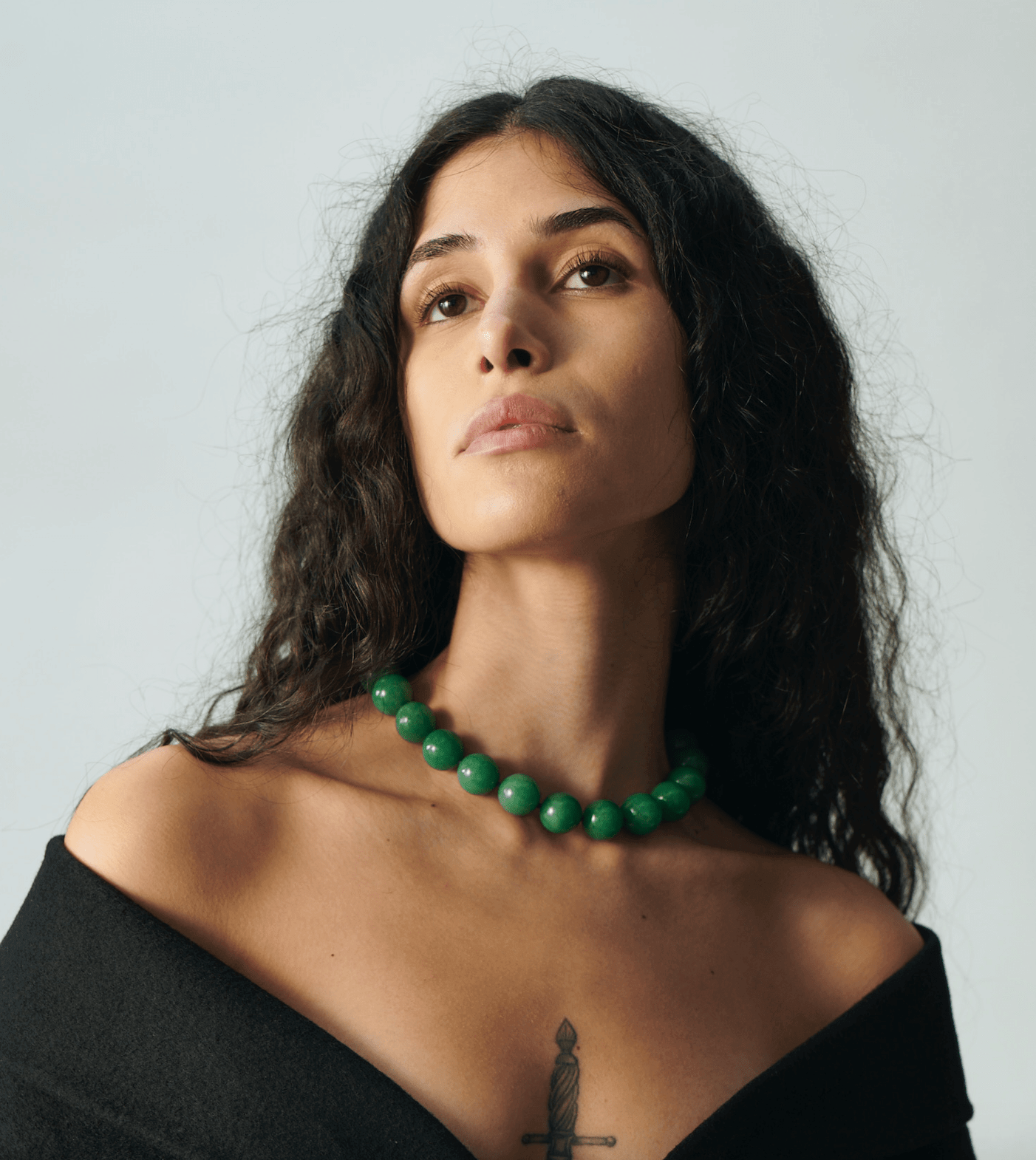 young woman with dark long curly hair wearing a big green gemstone necklace PRUM